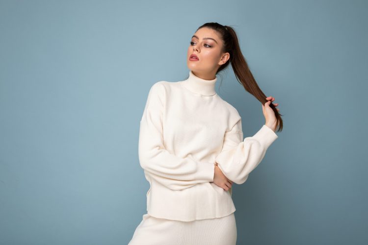 Lovely young woman wearing warm sweater standing isolated over blue background, posing.